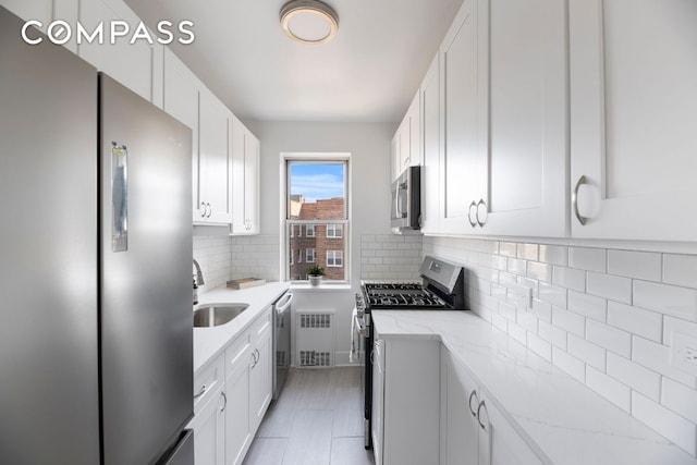 kitchen with appliances with stainless steel finishes, backsplash, light stone counters, white cabinets, and radiator