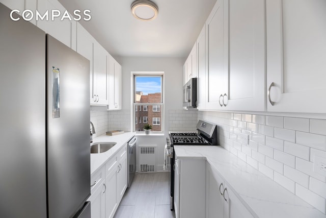 kitchen featuring appliances with stainless steel finishes, radiator, white cabinets, and decorative backsplash