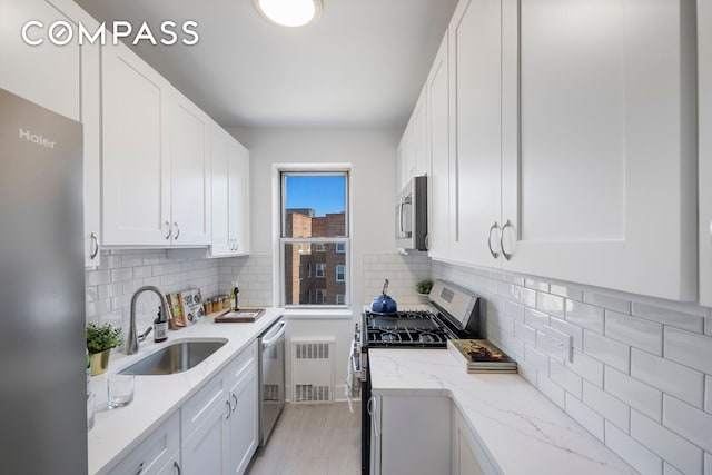 kitchen featuring a sink, stainless steel appliances, radiator heating unit, and white cabinets