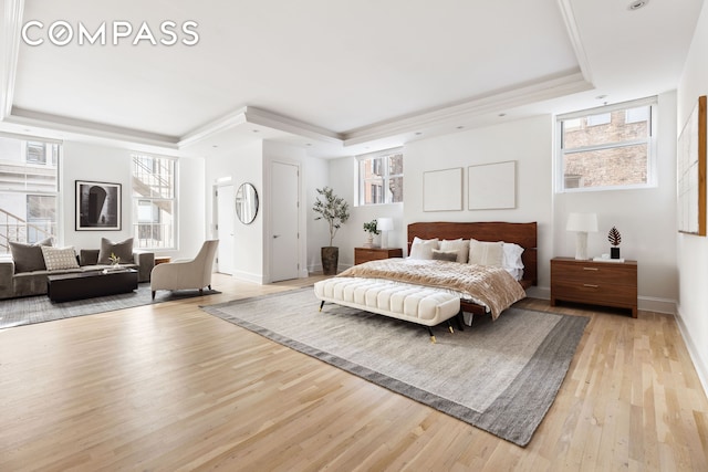 bedroom featuring a tray ceiling, multiple windows, and light wood-style floors