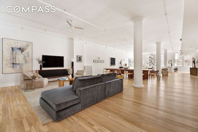 living area featuring light wood-type flooring, rail lighting, a ceiling fan, and ornate columns