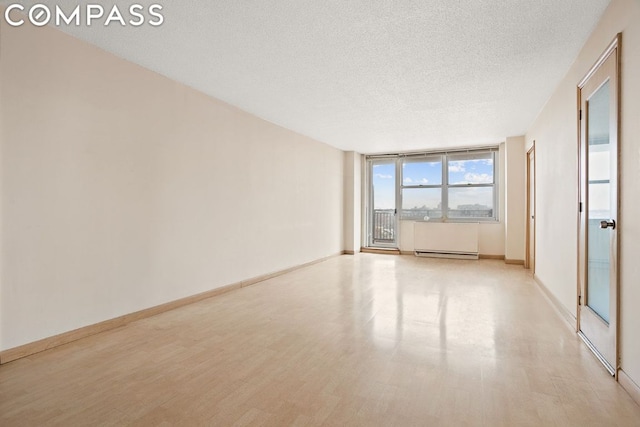 spare room featuring a textured ceiling, a baseboard heating unit, and light hardwood / wood-style flooring