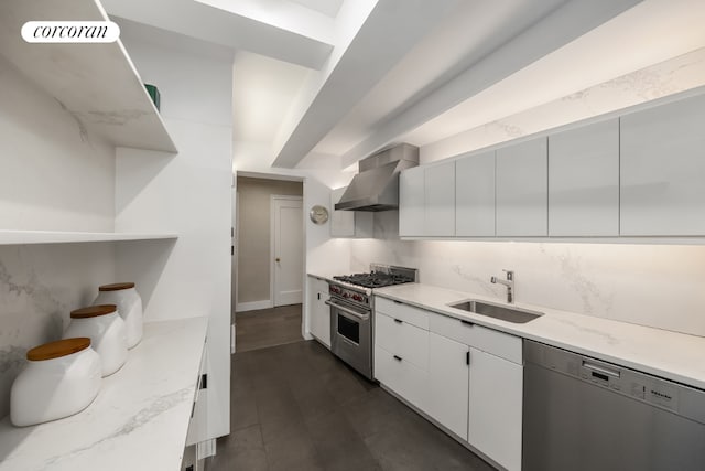 kitchen with stainless steel appliances, light stone counters, white cabinets, wall chimney range hood, and sink