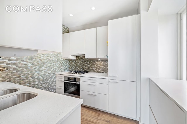 kitchen with sink, light hardwood / wood-style flooring, appliances with stainless steel finishes, backsplash, and white cabinets