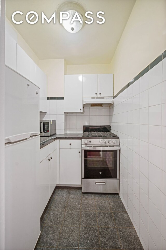 kitchen with granite finish floor, white cabinets, under cabinet range hood, appliances with stainless steel finishes, and tile walls