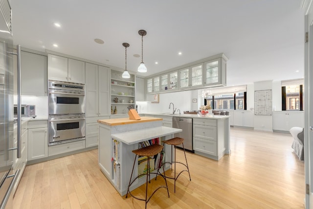 kitchen with appliances with stainless steel finishes, decorative light fixtures, light wood-type flooring, a kitchen island, and sink