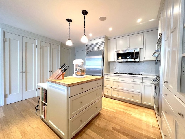 kitchen with wood counters, appliances with stainless steel finishes, pendant lighting, and white cabinetry