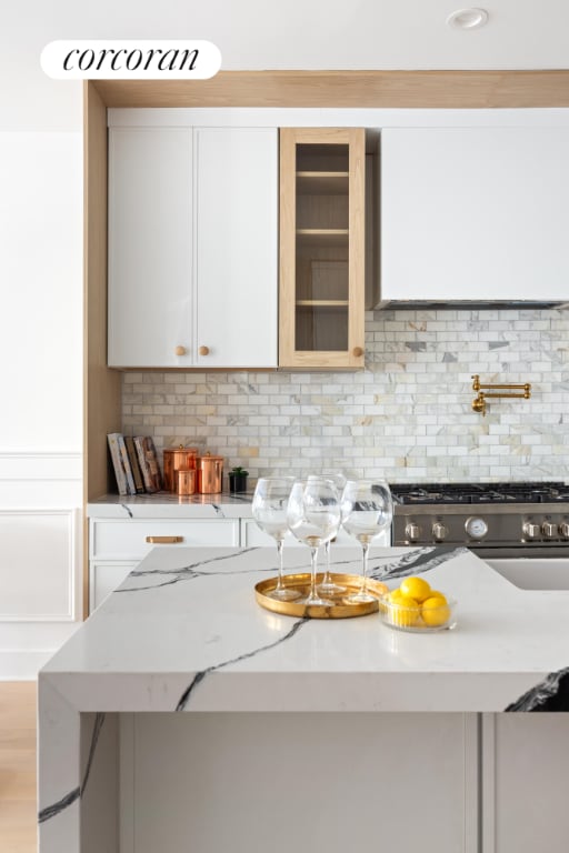 kitchen with decorative backsplash, light wood-type flooring, stainless steel gas range, white cabinets, and light stone counters