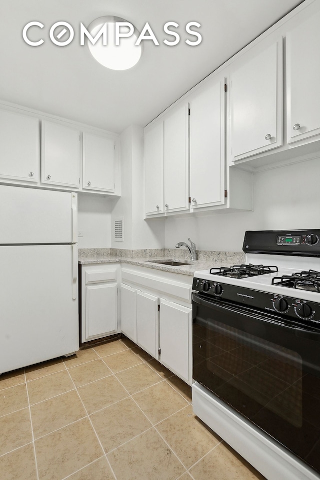 kitchen with gas range, light tile patterned floors, freestanding refrigerator, white cabinets, and a sink