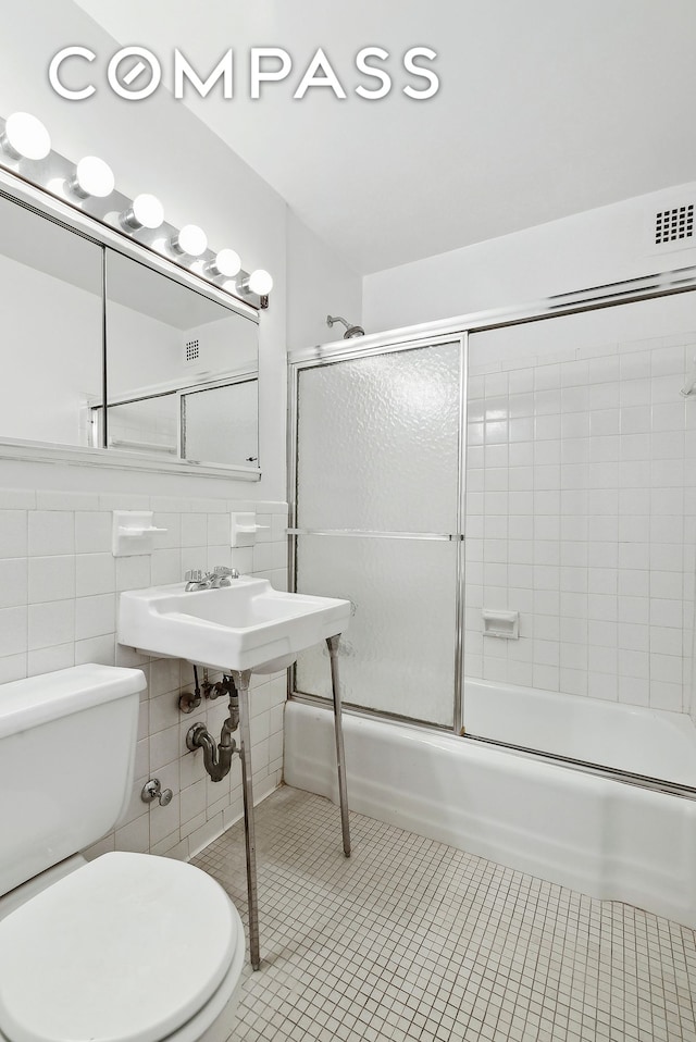 bathroom with tile patterned floors, toilet, tile walls, and bath / shower combo with glass door