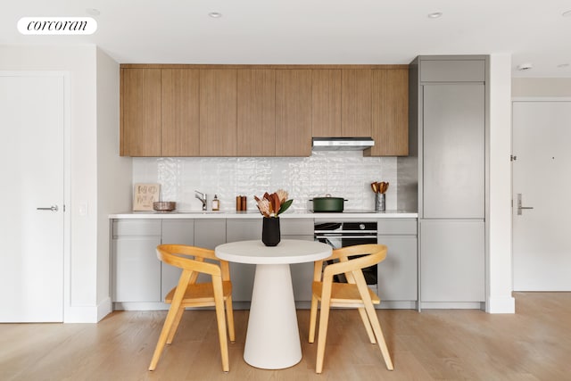 kitchen with wall oven, visible vents, light wood-style floors, and under cabinet range hood