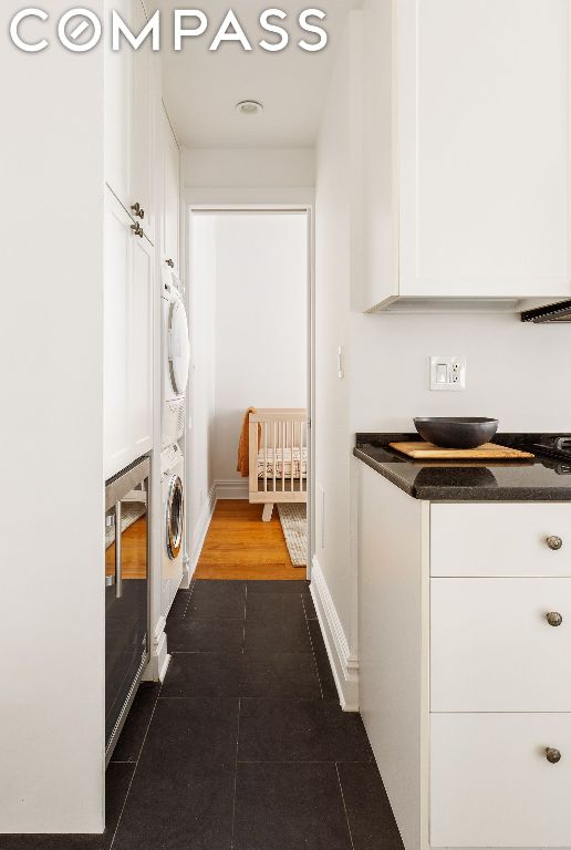 washroom with cabinets, dark tile patterned flooring, and stacked washer / drying machine