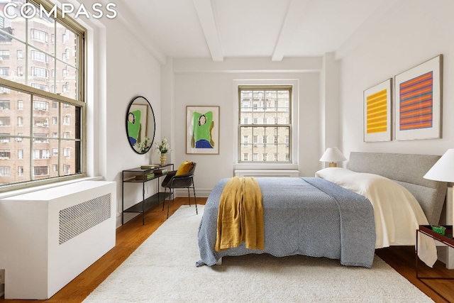 bedroom with beamed ceiling, wood-type flooring, and radiator heating unit