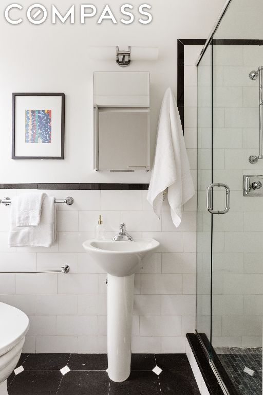 bathroom featuring tile patterned floors, tile walls, toilet, and an enclosed shower