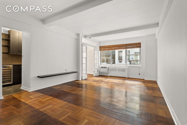 unfurnished living room with wine cooler, radiator heating unit, dark parquet floors, and beamed ceiling