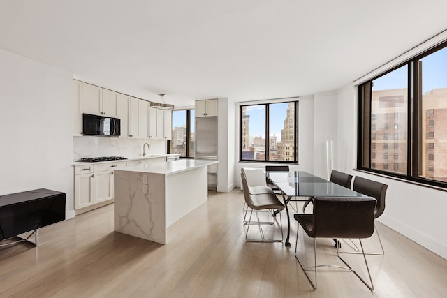 kitchen with black microwave, a kitchen island, light wood-style floors, light countertops, and decorative backsplash