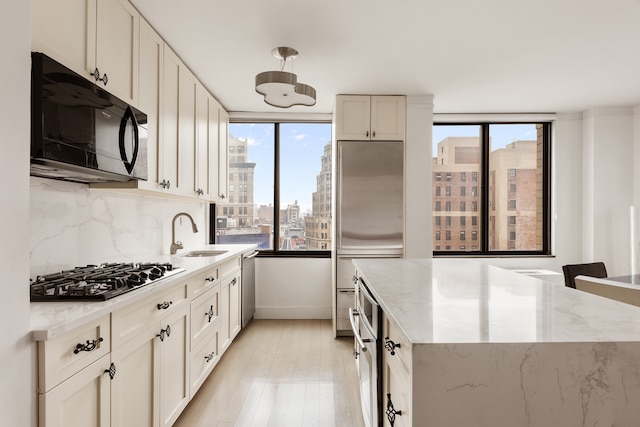 kitchen with light wood-style flooring, a city view, stainless steel appliances, a sink, and backsplash