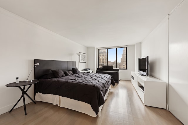 bedroom with baseboards, crown molding, and light wood finished floors