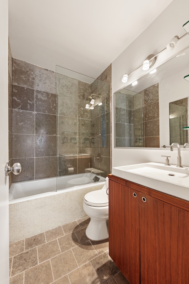 full bathroom featuring stone finish flooring, tiled shower / bath combo, vanity, and toilet