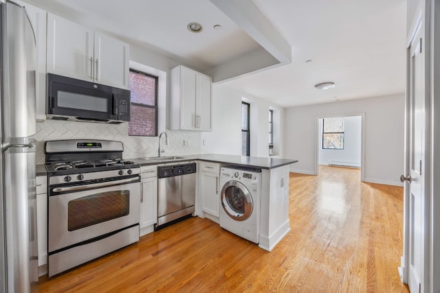 kitchen featuring sink, appliances with stainless steel finishes, kitchen peninsula, washer / clothes dryer, and white cabinets