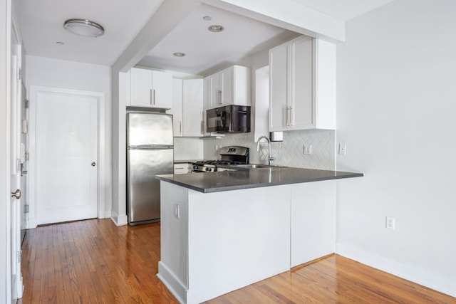 kitchen with decorative backsplash, appliances with stainless steel finishes, a peninsula, wood finished floors, and a sink