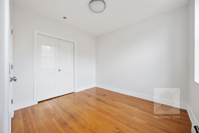 unfurnished bedroom featuring a baseboard radiator, baseboards, a closet, and light wood finished floors