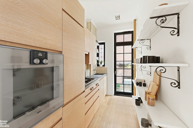 kitchen featuring light brown cabinets, light countertops, ornamental molding, light wood-type flooring, and tasteful backsplash