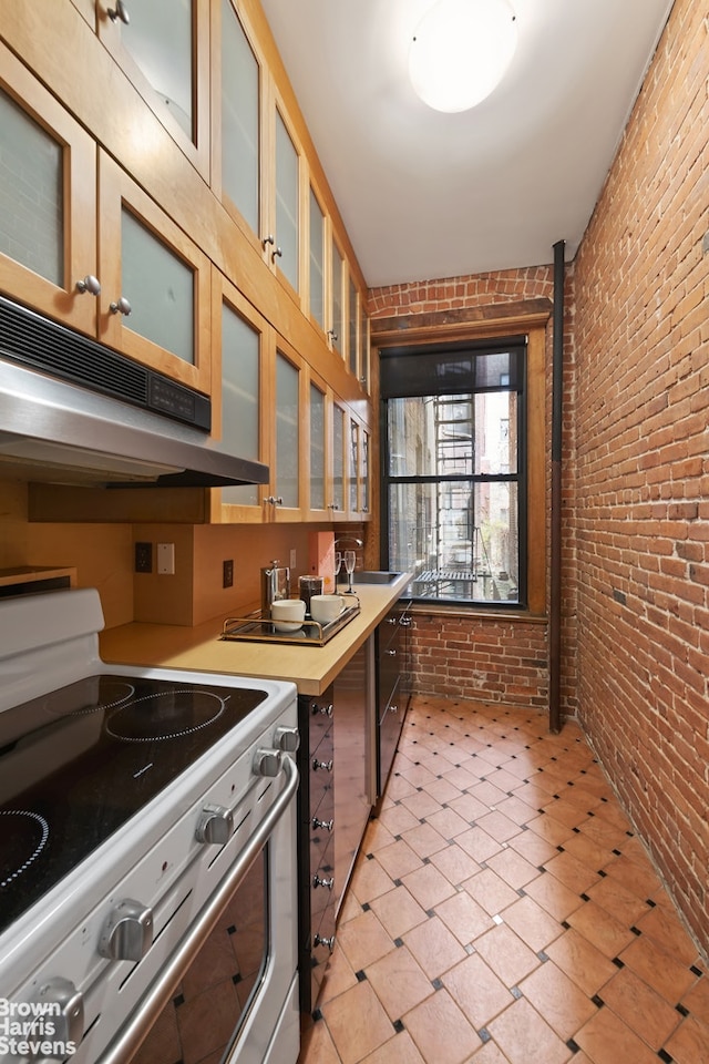 kitchen featuring under cabinet range hood, white electric range, brick wall, light countertops, and glass insert cabinets