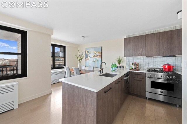 kitchen featuring kitchen peninsula, tasteful backsplash, high end range, dark brown cabinetry, and sink