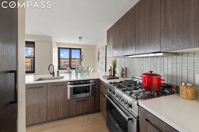 kitchen with stainless steel appliances, sink, backsplash, kitchen peninsula, and dark brown cabinets