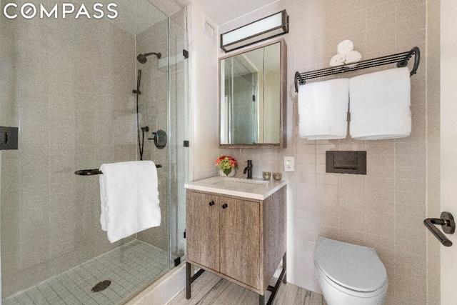 bathroom with toilet, tile walls, a shower with shower door, and vanity