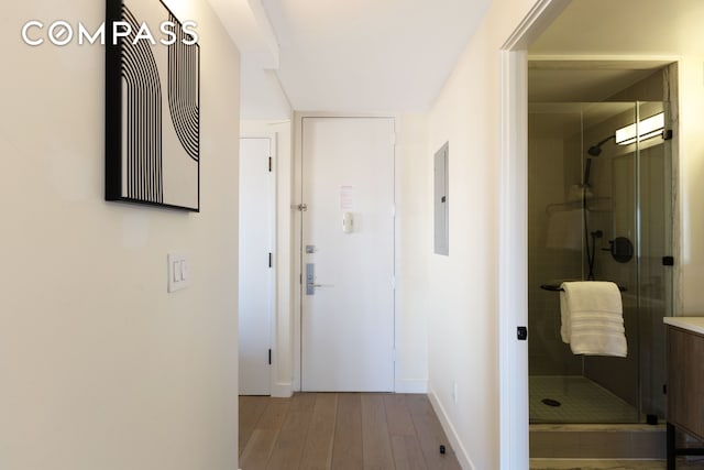 corridor featuring wood finished floors, baseboards, and electric panel