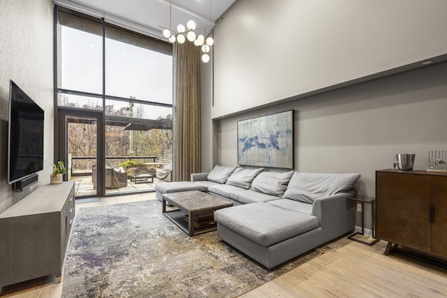 living area featuring a chandelier, light wood-type flooring, floor to ceiling windows, and a towering ceiling