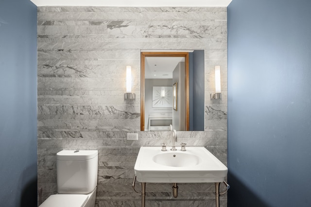 bathroom featuring a sink, toilet, and tile walls