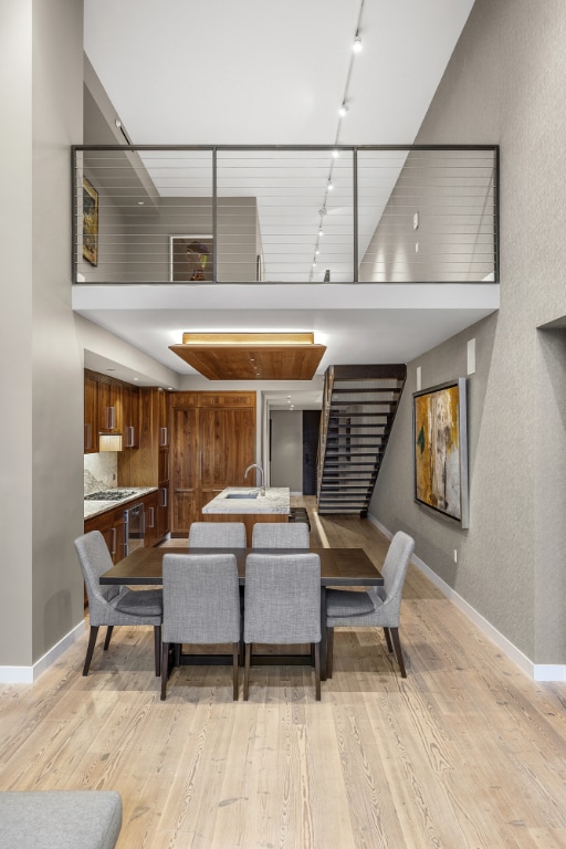 dining room with a towering ceiling, baseboards, stairway, light wood-type flooring, and track lighting