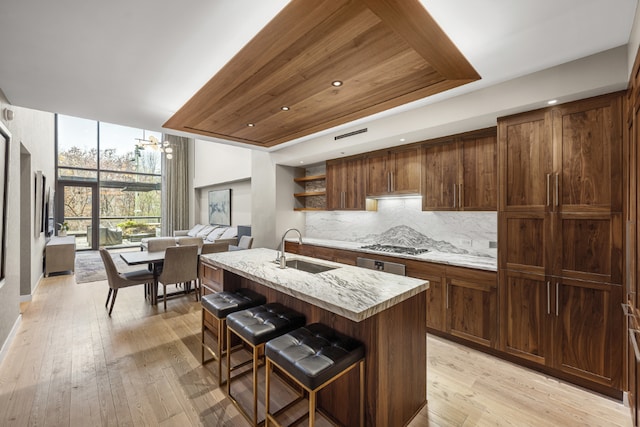 kitchen with a breakfast bar area, backsplash, light wood-style floors, a sink, and an island with sink