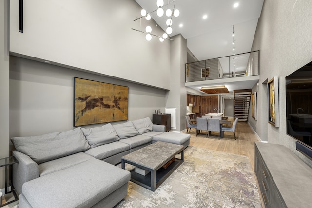 living room with baseboards, a notable chandelier, a towering ceiling, and light wood-style floors