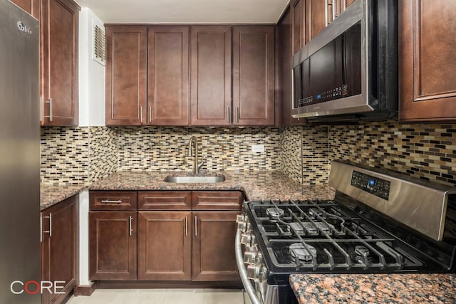 kitchen featuring appliances with stainless steel finishes, light stone countertops, sink, and backsplash