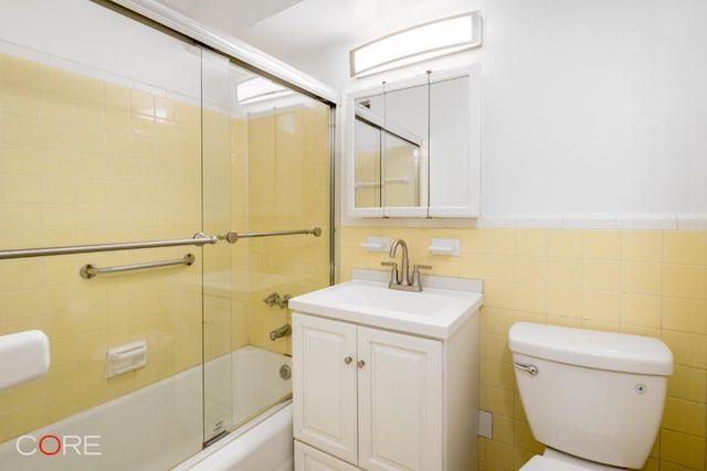 full bathroom featuring vanity, toilet, combined bath / shower with glass door, and tile walls