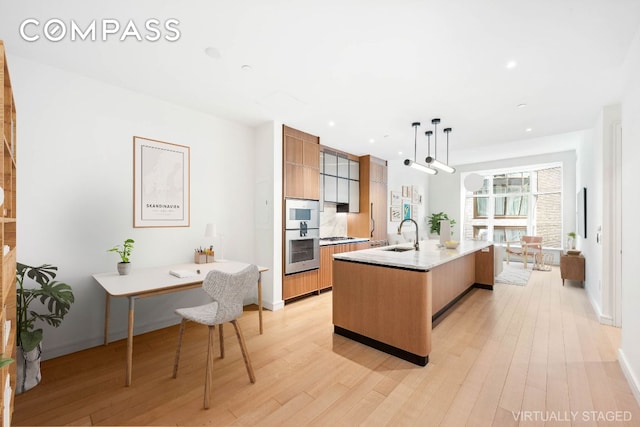 kitchen with pendant lighting, sink, light hardwood / wood-style floors, and a center island with sink