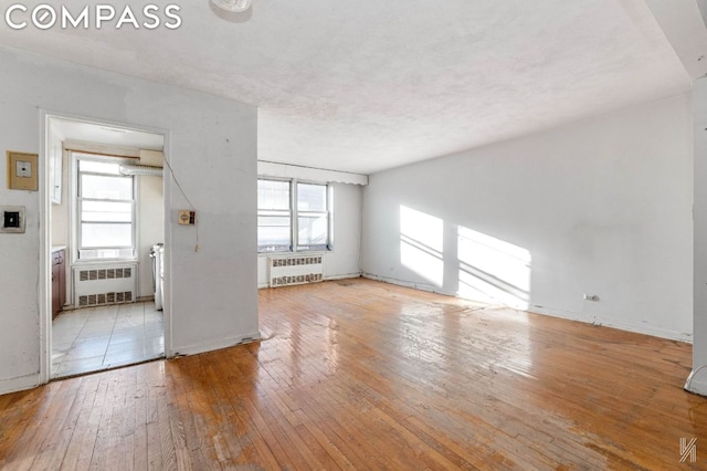 unfurnished living room featuring a textured ceiling, radiator, and light hardwood / wood-style flooring