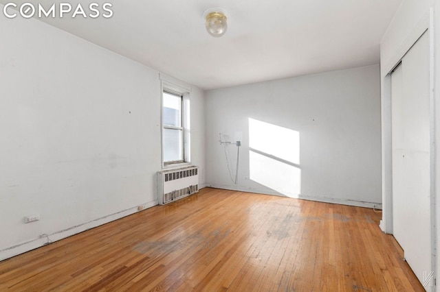 unfurnished bedroom featuring radiator heating unit, a closet, and light wood-type flooring