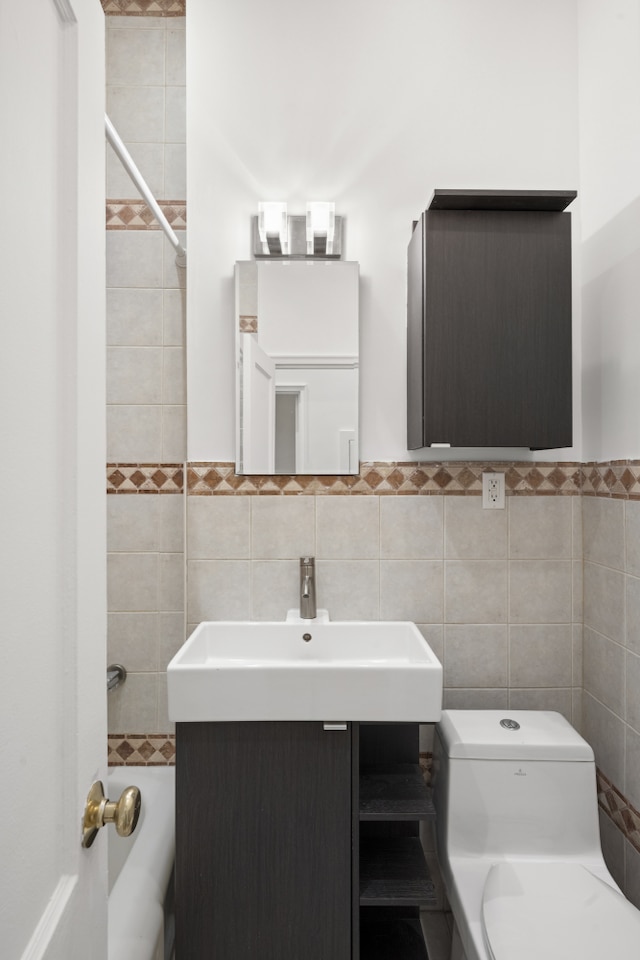 bathroom with a sink, tile walls, wainscoting, and toilet