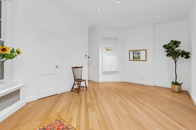 unfurnished room featuring arched walkways, built in features, recessed lighting, baseboards, and light wood-type flooring
