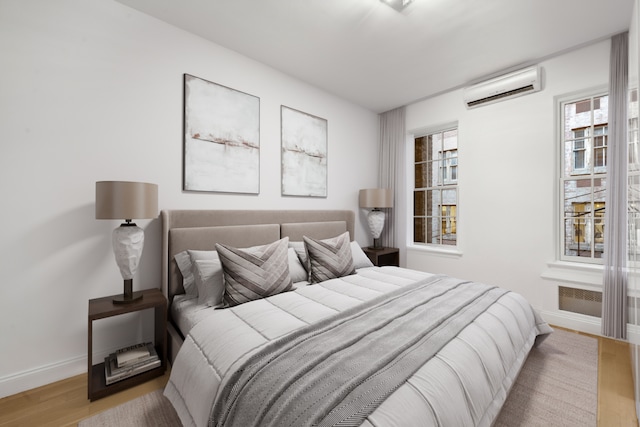 bedroom with wood finished floors, baseboards, and a wall mounted AC
