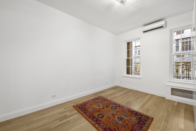 unfurnished room with baseboards, light wood finished floors, and a wall mounted air conditioner