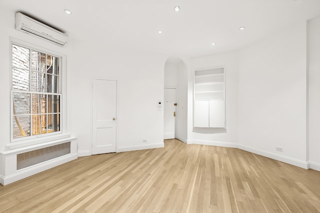 unfurnished room with a wall unit AC, arched walkways, light wood-type flooring, baseboards, and recessed lighting