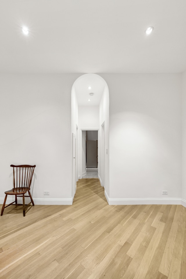 unfurnished room featuring recessed lighting, baseboards, light wood finished floors, and arched walkways