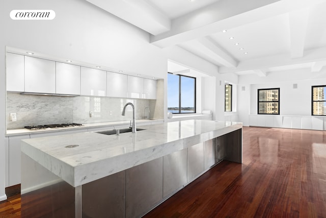 kitchen featuring beamed ceiling, dark wood-type flooring, a sink, white cabinets, and light stone countertops