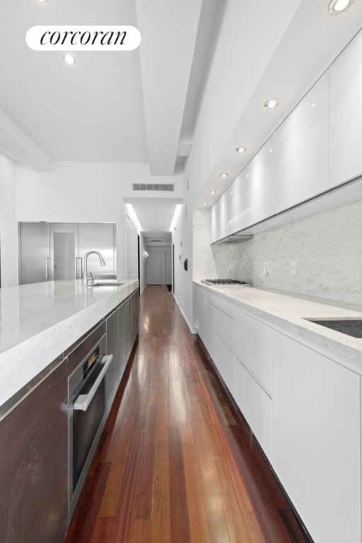 kitchen with tasteful backsplash, white cabinets, modern cabinets, stainless steel oven, and a sink